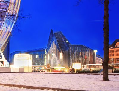 Foto: Seitliche Ansicht auf das Hauptgebäude der Universität am Campus Augustusplatz in weihnachtlicher Atmosphäre und Lichterbogen vom Riesenrad.