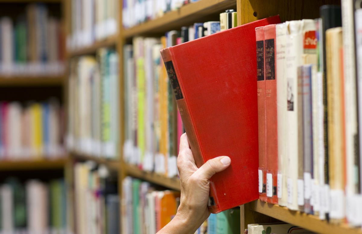 zur Vergrößerungsansicht des Bildes: Hand zieht ein rotes Buch aus einem Bücherregal