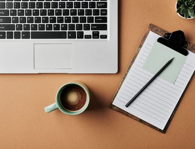 Eine Tasse Kaffee steht neben einem Laptop und einem Block