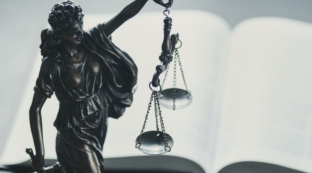 Statue der Justitia, neben ihr liegt ein aufgeschlagenes Buch.