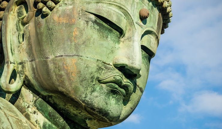 Nahaufnahme des Gesichtes einer alten japanischen Statue. Im Hintergrund ist der Himmel zu sehen.