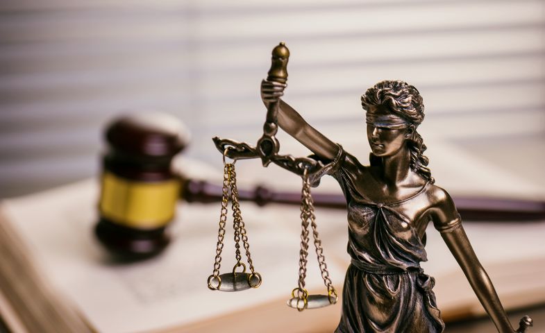 Figur der Justitia vor einem Richterhammer auf einem Buch