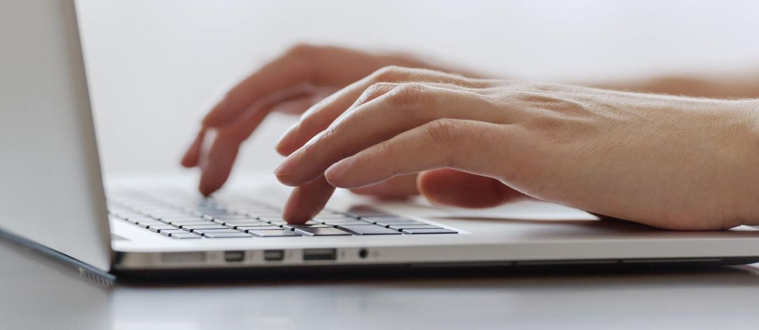 Weibliche Hände tippen auf einem Laptop.