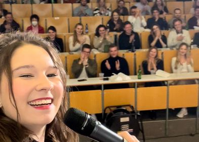 Bei ihren Slam-Auftritten nimmt Elli auch typische Situationen im Studium aufs Korn, Foto: privat Elisabeth mit einem Mikrofon vor Publikum in einem Hörsaal