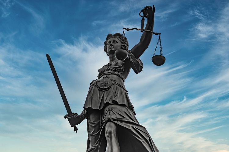 Statue von Justitia mit Waage und Schwert vor einem blauen Himmel