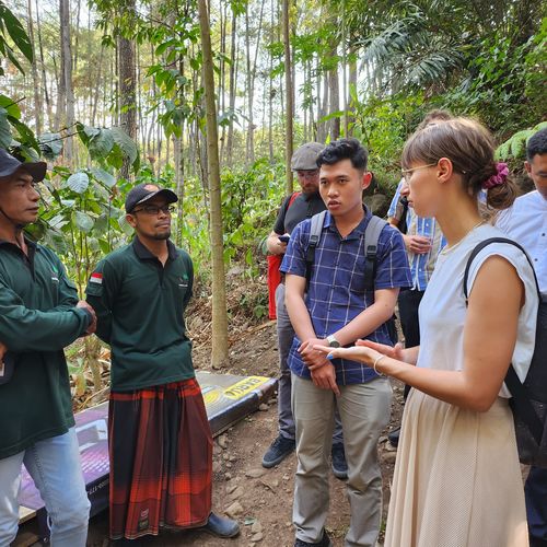 Die Teilnehmenden des Workshops beim Besuch einer Kaffeeplantage. Vier Personen unterhalten sich. Im Hintergrund sind Bäume zu sehen.