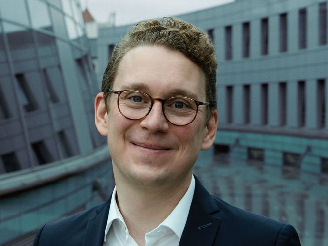 Mann mit kurzen blonden Haaren und Brille schaut freundlich in die Kamera