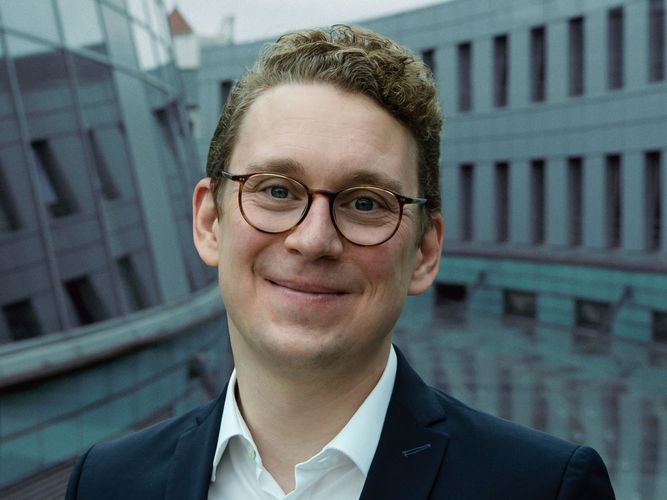 Mann mit kurzen blonden Haaren und Brille schaut freundlich in die Kamera