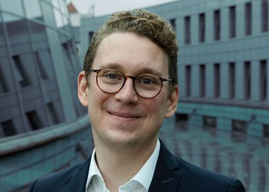 Mann mit kurzen blonden Haaren und Brille schaut freundlich in die Kamera