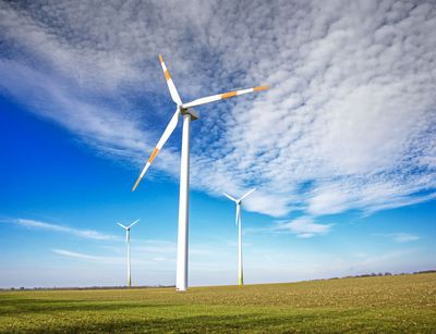 Drei Windräder auf einem großen Feld, darüber blauer Himmel mit kleinen Wolken.