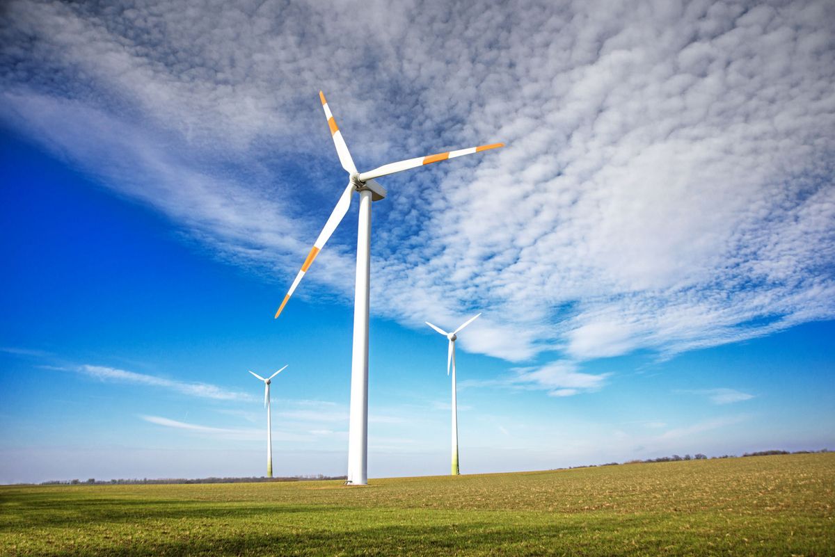 enlarge the image: Drei Windräder auf einem großen Feld, darüber blauer Himmel mit kleinen Wolken.