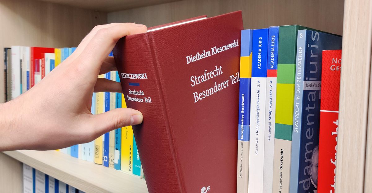 zur Vergrößerungsansicht des Bildes: Das Lehrbuch "Strafrecht Besonderer Teil" von Prof. Klesczewski wird aus einem Bücherregal genommen