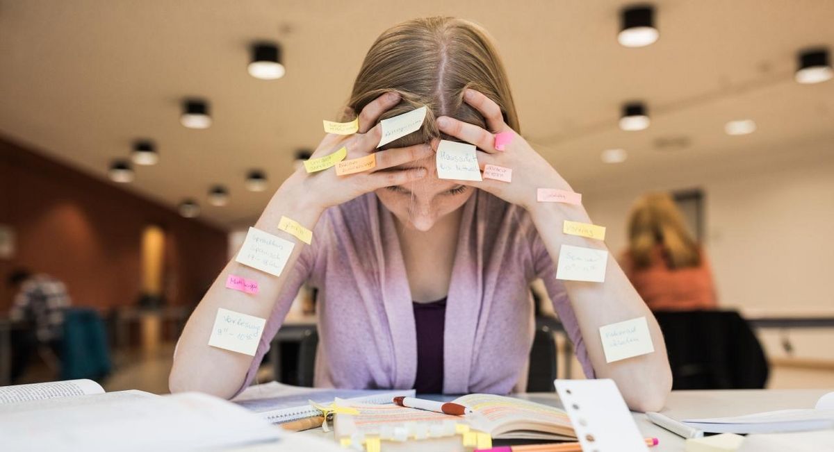 zur Vergrößerungsansicht des Bildes: Studentin beim angestrengten Lernen. Sie stützt den Kopf in die Hände, an ihren Armen kleben Post-its.