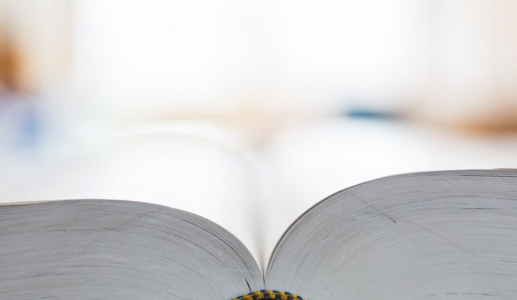 Ein in der Mitte aufgeschlagenes Buch liegt auf dem Tisch.