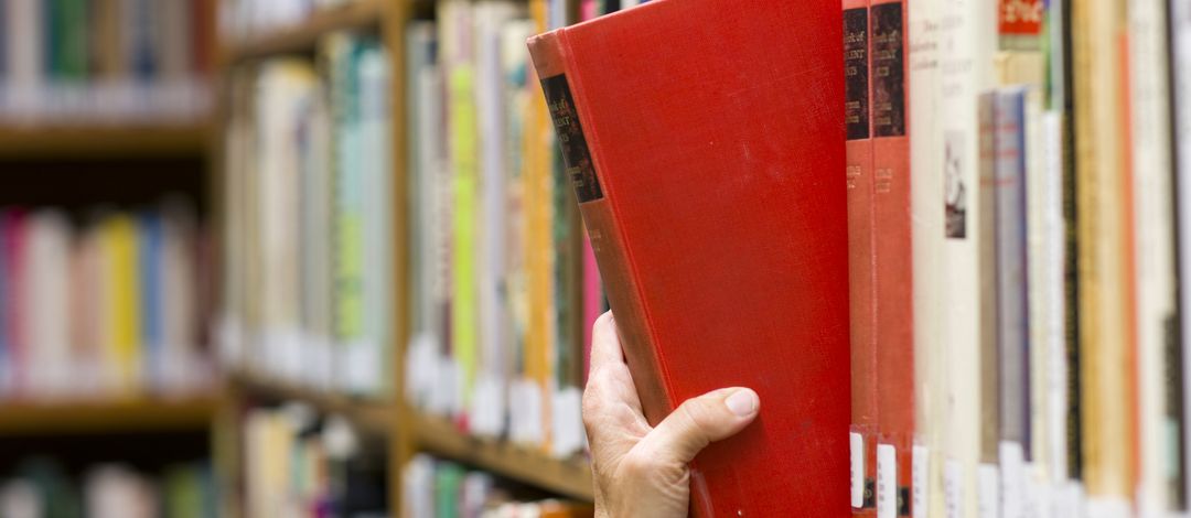 Eine Hand nimmt ein Buch aus einem Regal, Foto: Colourbox