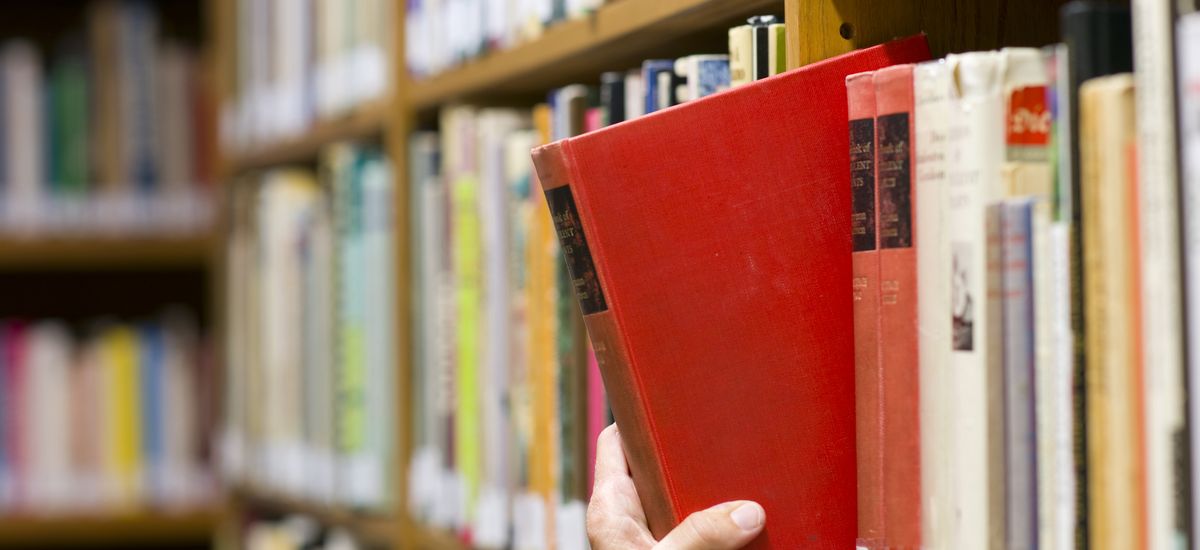Hand zieht ein rotes Buch aus einem Bücherregal