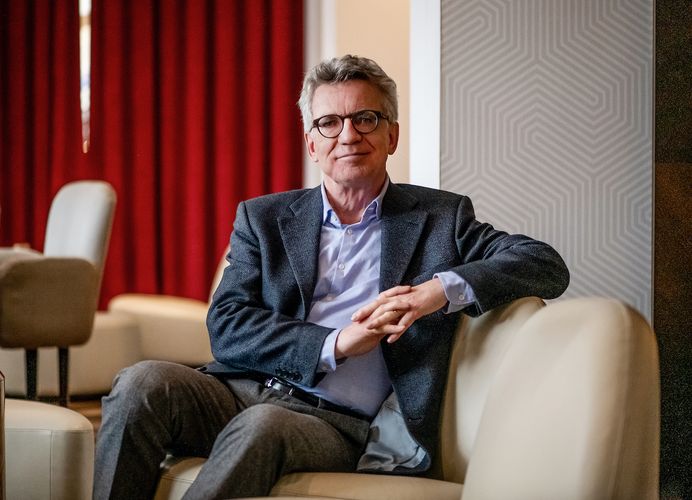 Portraitfoto von Prof. Dr. Thomas de Maizière; auf einer beigen Couch vor rotem Vorhang sitzend mit Blick in die Kamera; Foto: www.thomasdemaiziere.de