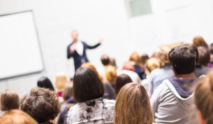 zeigt Gruppe von Studierenden vor einem Dozierenden in einem Hörsaal