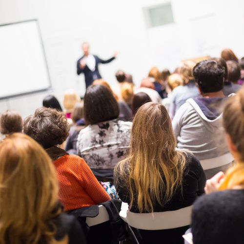 zeigt eine Gruppe von Studierenden vor einem Dozenten im Hörsaal