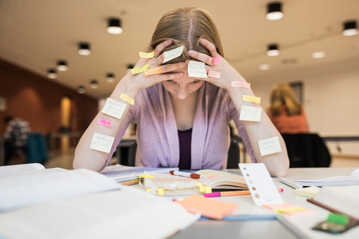 zur Vergrößerungsansicht des Bildes: Studentin beim angestrengten Lernen. Sie stützt den Kopf in die Hände, an ihren Armen kleben Post-its.