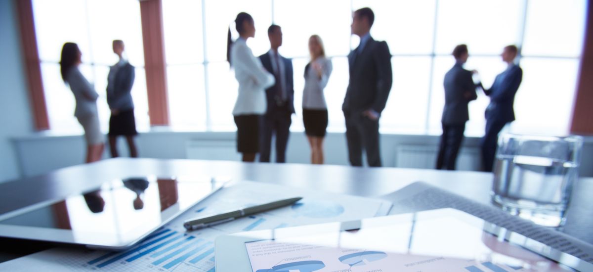 Büro mit Schreibtisch mit Dokumenten im Vordergrund, im Hintergrund, Menschen, die sich besprechen