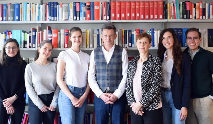 Gruppenfoto des Lehrstuhlteams. V.l.n.r: Helena Ferber, Lea Stanescu, Antonia Vonnahme, Christian Berger, Andrea Kuntzsch, Luisa Schmidt, Florian Wundrich Hintergrund: Bücherregal mit juristischer Fachliteratur