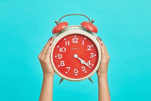 Bunte Standuhr von zwei Händen in die Luft gehalten